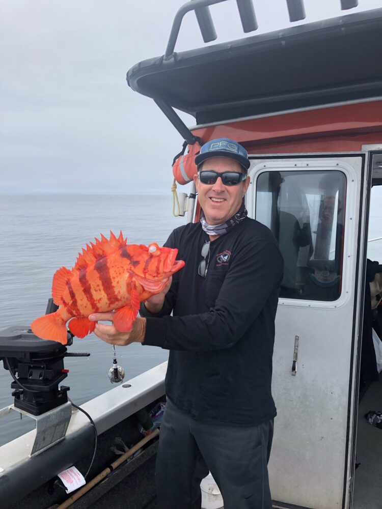 Guest fisherman holding a rockfish on a Queen Charlotte Safaris boat