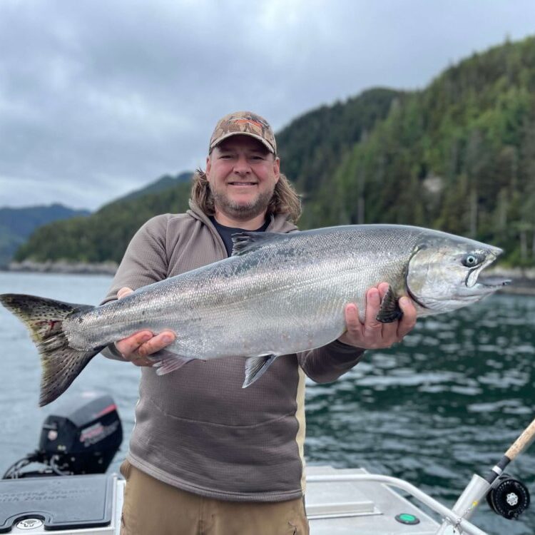 Guest fisherman holding a Chinook salmon on a Queen Charlotte Safaris boat